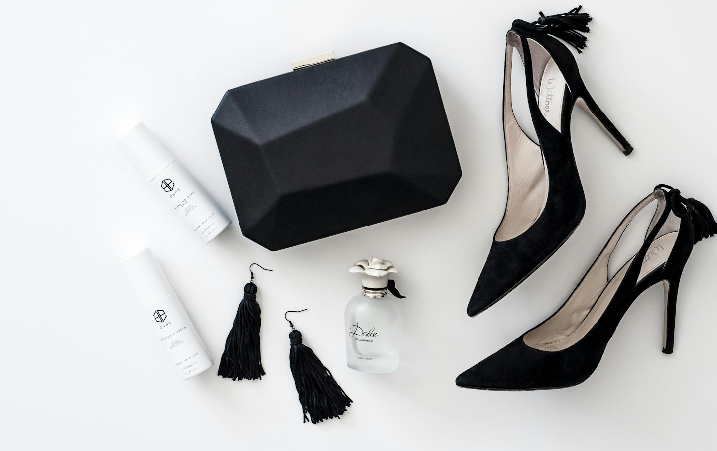 Scarpe col tacco nere, pochette, prodotti di bellezza e orecchini.