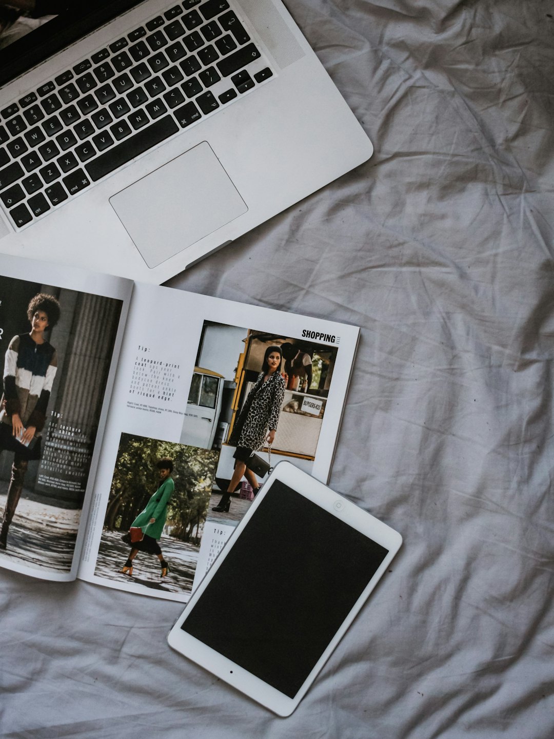 Laptop, tablet e rivista di moda su tessuto grigio.
