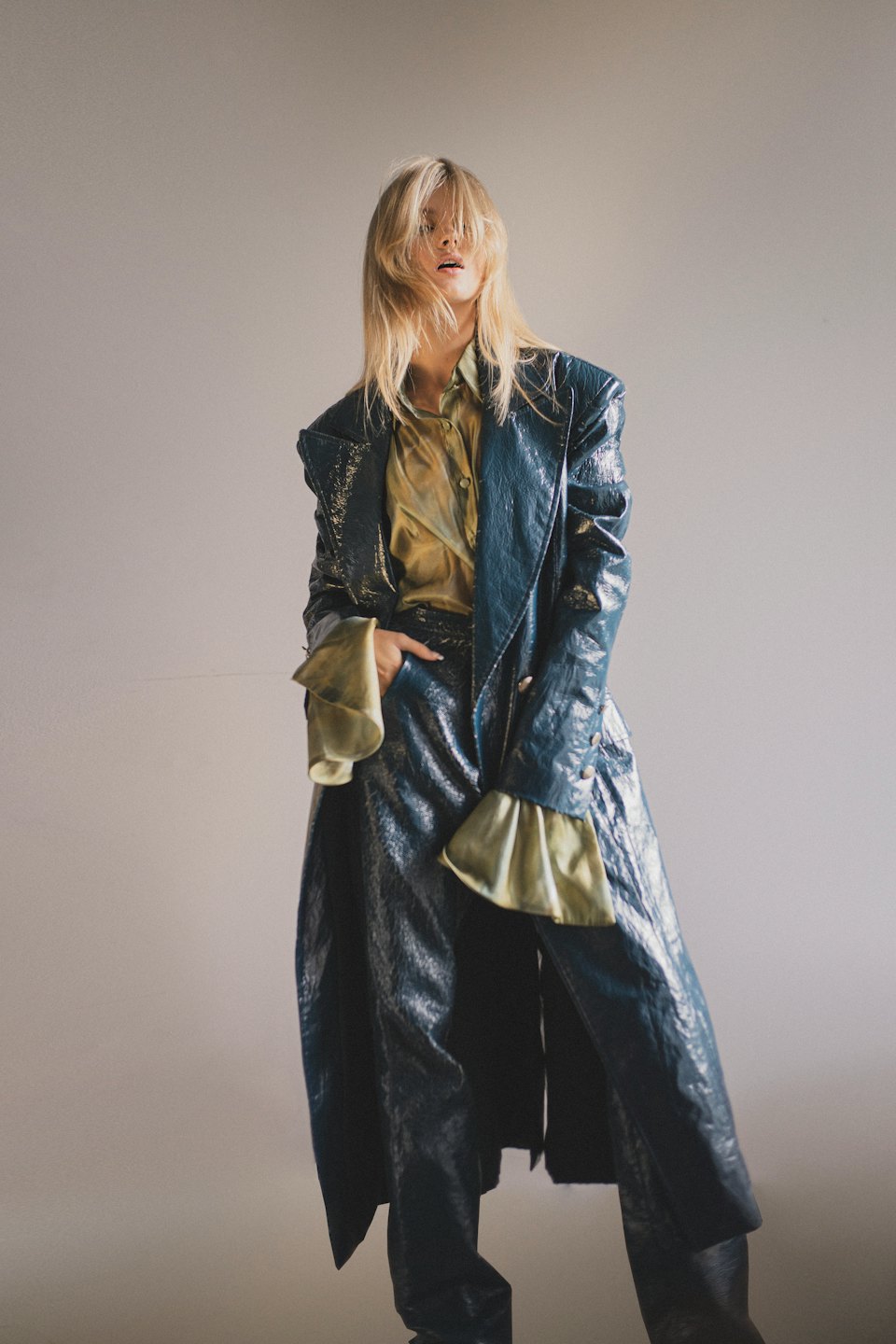 Donna con cappotto e pantaloni in pelle color petrolio in posa in studio.