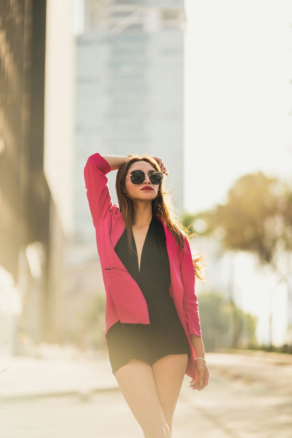 Donna con blazer fucsia in posa sul marciapiede di una città.